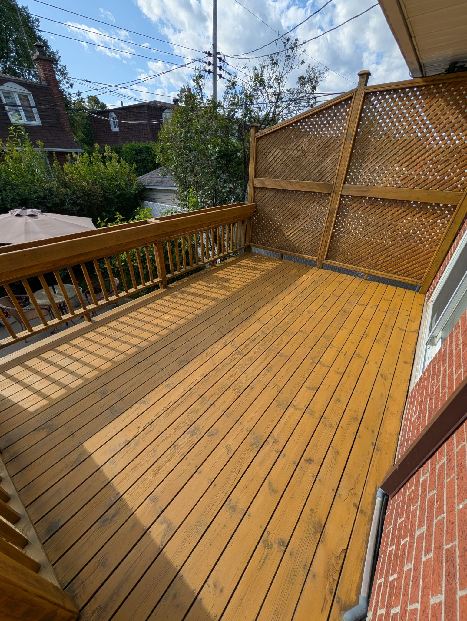 Wooden deck with a lattice privacy screen along a brick house overlooking trees and power lines against a blue sky  Bricopro  Bricopro