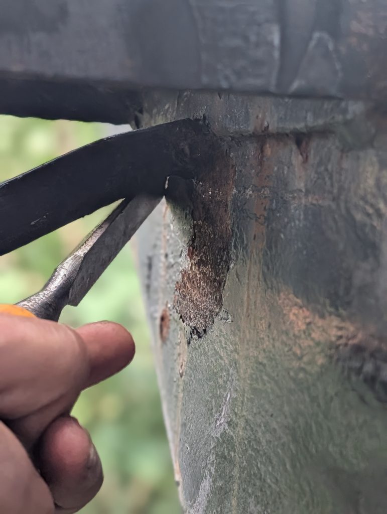 Close up of a rusted metal joint with flaking paint a finger pointing at a crack between two metal plates  Bricopro  Bricopro